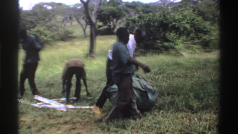 Men work together in the grass, with one bending near a low frame while others guide the green tarp.