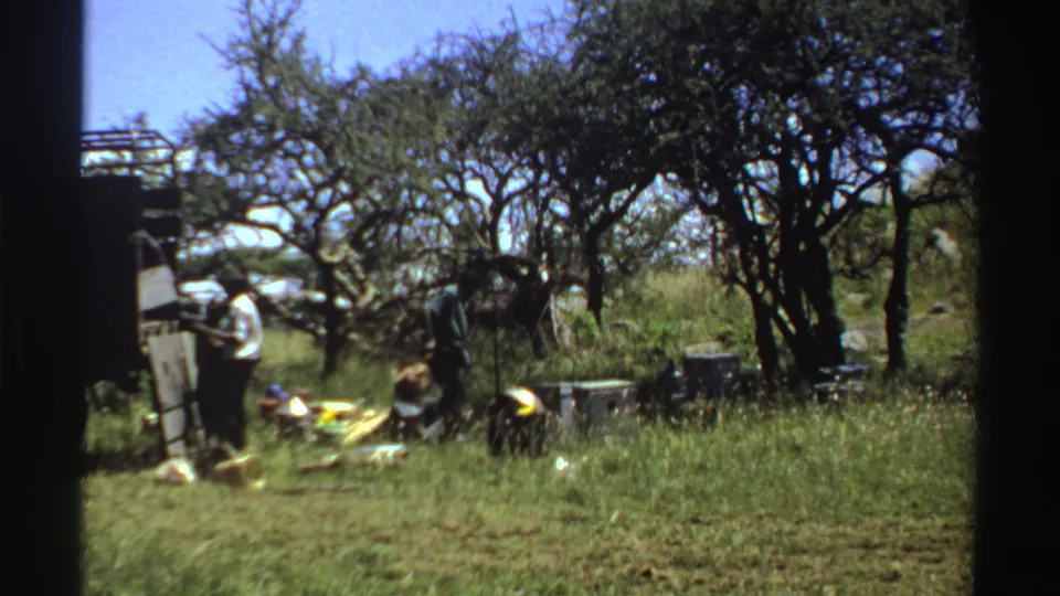 1969 Nigeria 8mm frame showing a man bending near supplies as others stand beside a truck in grassland.