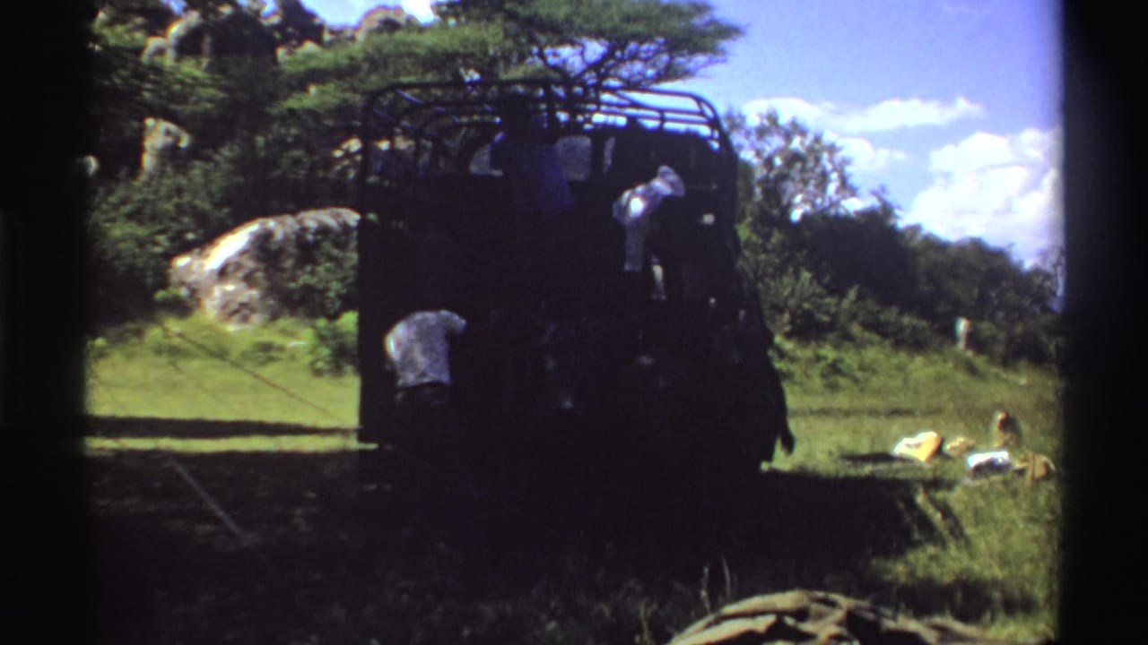 People unload or arrange supplies around a rugged truck in a bright Nigerian savanna scene from 1969 8mm footage.