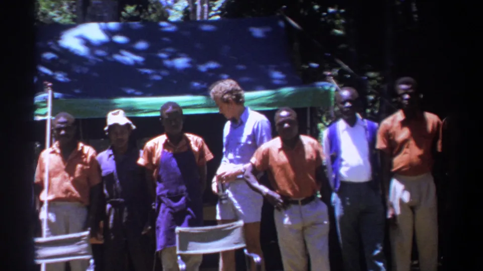A visitor group in Kenya stands near a chair and canopy, with 1960s clothing visible in the 8mm frame.
