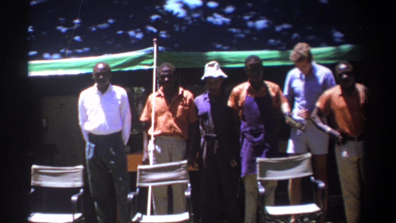 Adult men pose outdoors near white chairs beneath a green canopy.