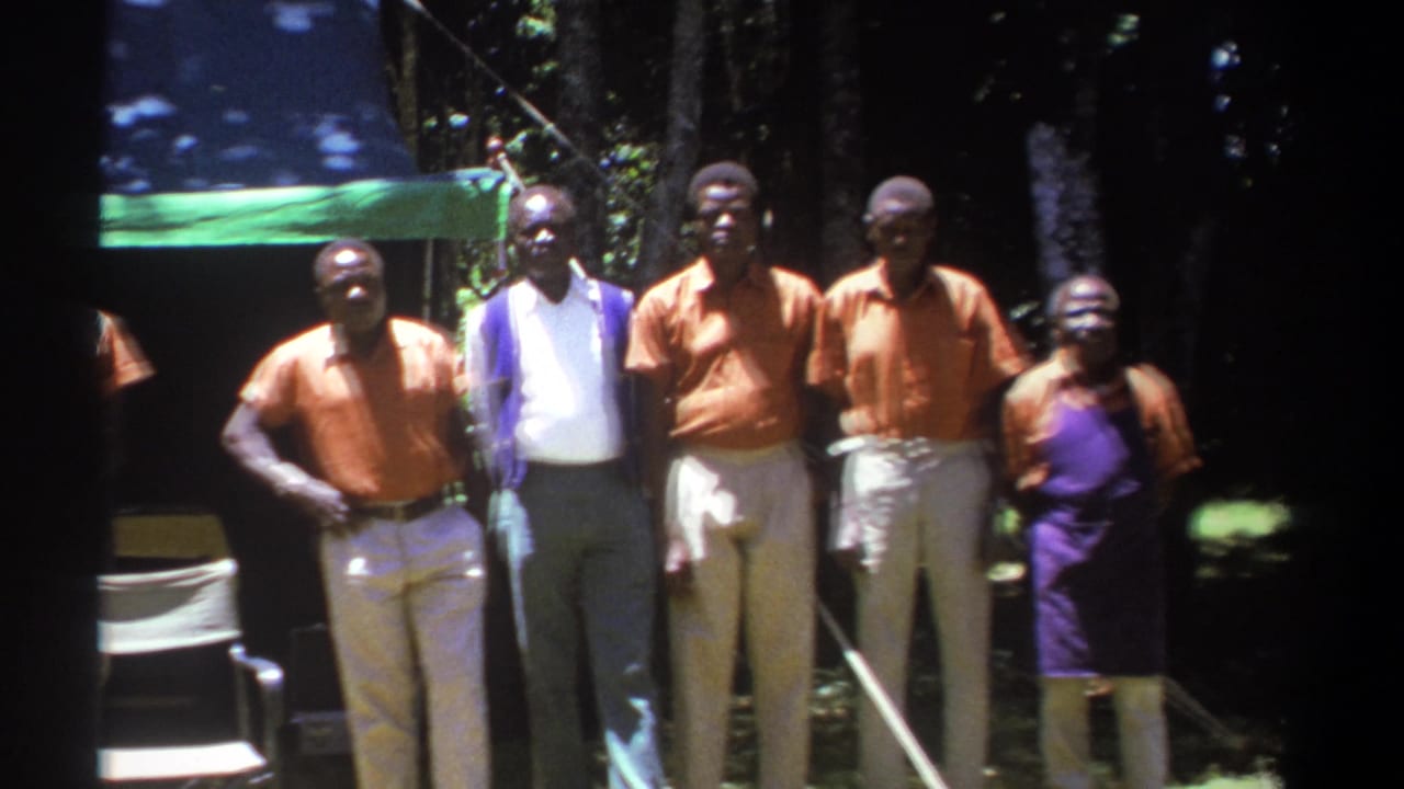 Group of adults pose near a green canopy with a folding chair partly visible.