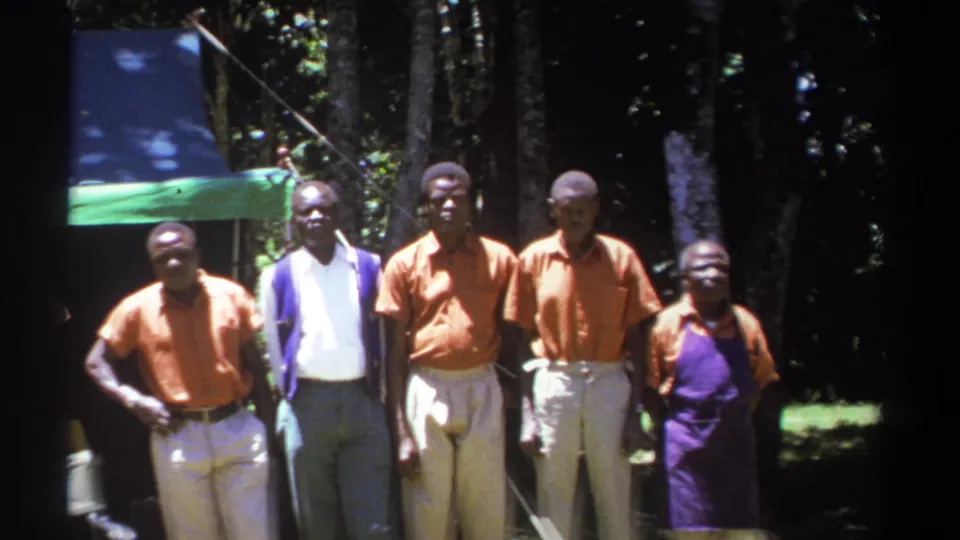 Five Black men appear in a looser outdoor lineup in Kenya, with orange shirts, light trousers, purple clothing, and trees behind them.