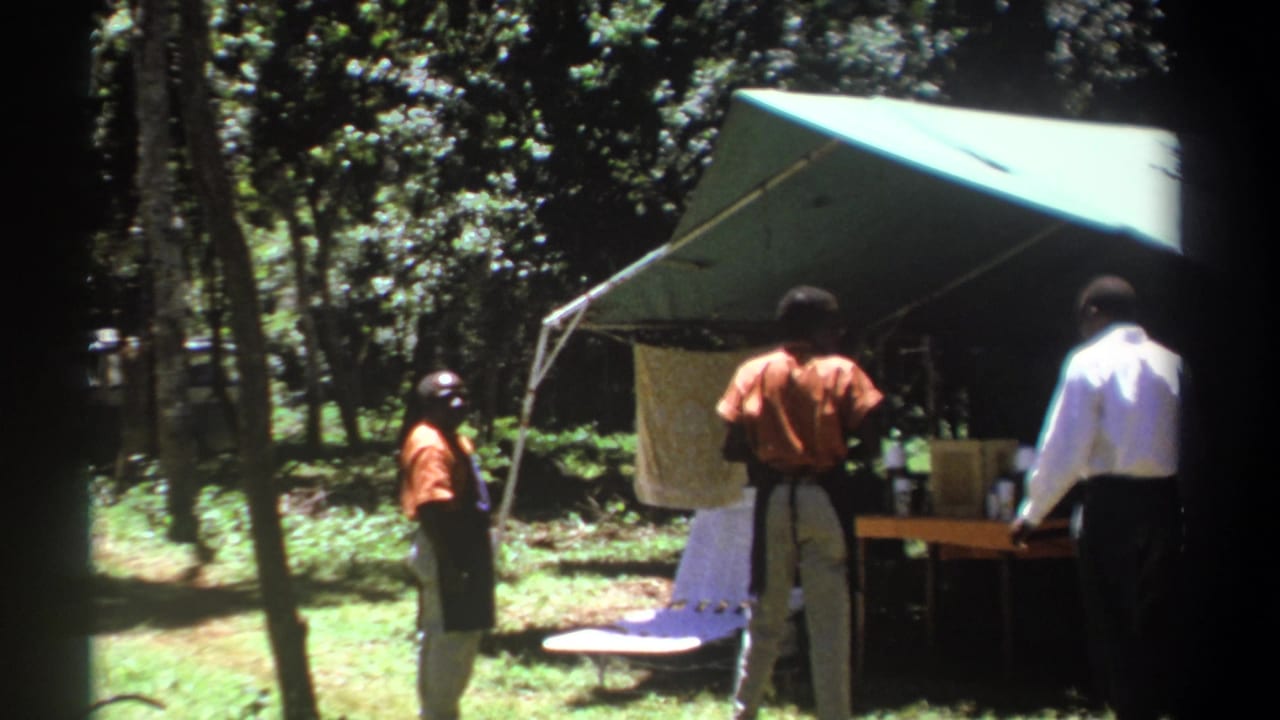 Men stand near a green canvas tent in a wooded campsite.