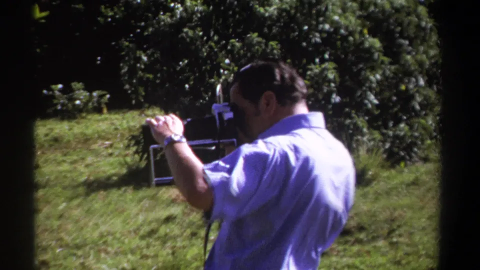The man continues handling the vintage 8mm camera in a wooded grassy area, with the Kenya 1969 context supplied by clip metadata.