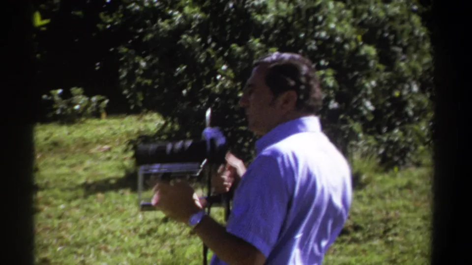 In the final frame, the man turns slightly while holding the vintage 8mm camera against a backdrop of grass and foliage in Kenya-dated 1969 footage.