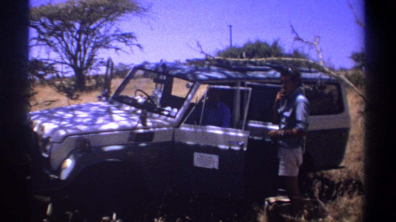 Man standing beside a dark off-road vehicle in dry savanna terrain.