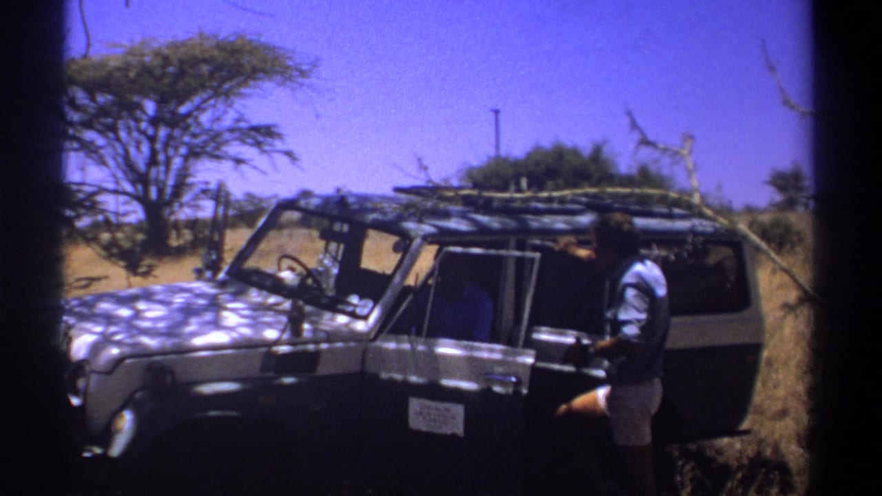 Man standing beside an open 4x4 safari vehicle door in dry savanna terrain.