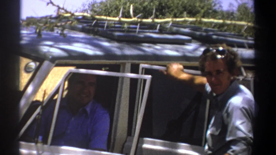 1969 Kenya home-movie frame showing the open cabin of a safari vehicle, one man inside, and another at the side.