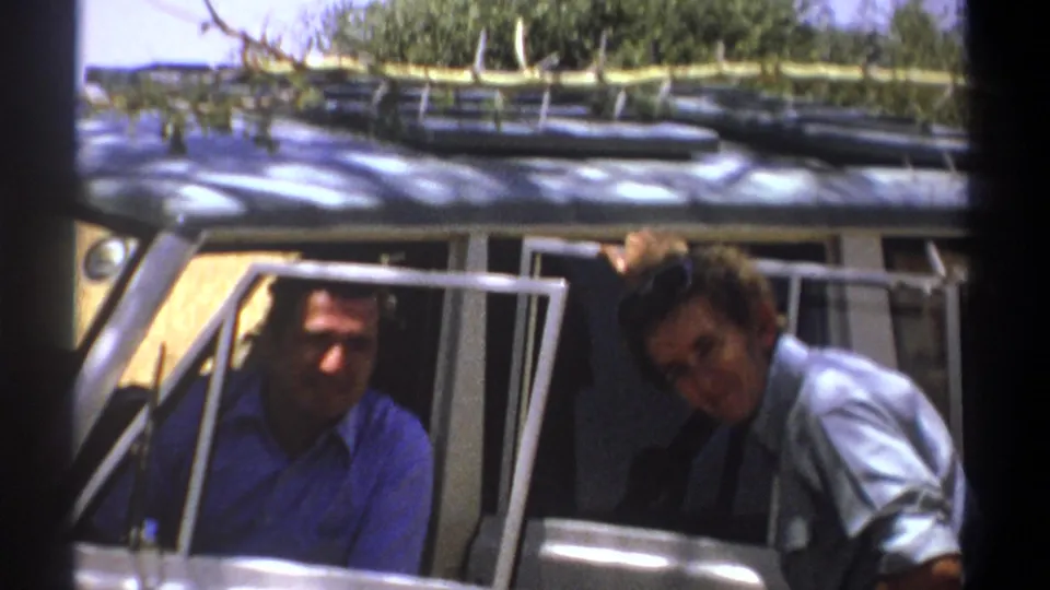 1969 Kenya frame showing two men at a safari vehicle, with one smiling from inside and one leaning near the door.