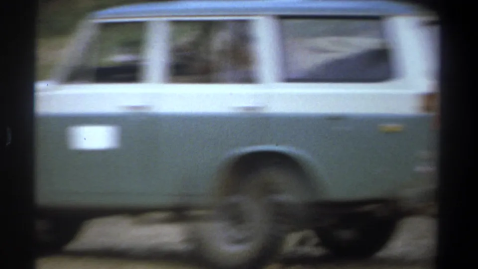 A green and white safari vehicle moves through the frame in the 1969 Kenya roadside safari scene.