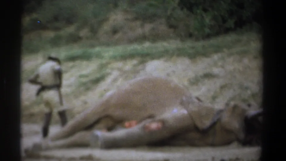 1969 Kenya 8mm frame showing a uniformed forest police officer approaching the dead elephant lying in a dusty clearing.