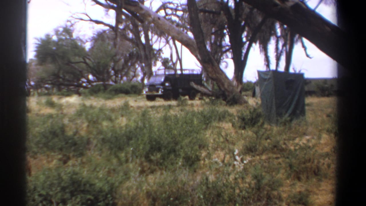 Dark jeep parked near a green canvas tent under large trees in a dry field.