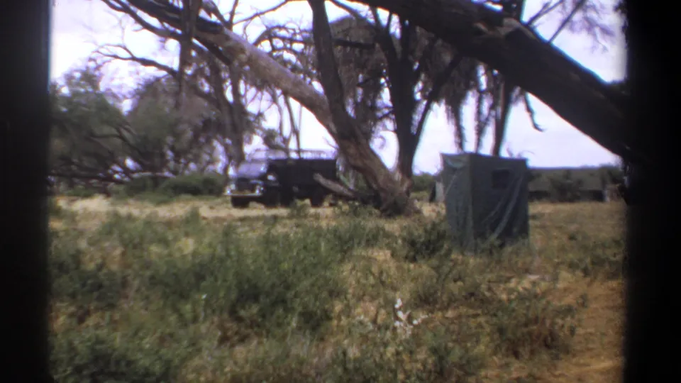 Final 1969 Kenya safari-camp frame showing a dark jeep, green tent, dry grass and spreading trees.