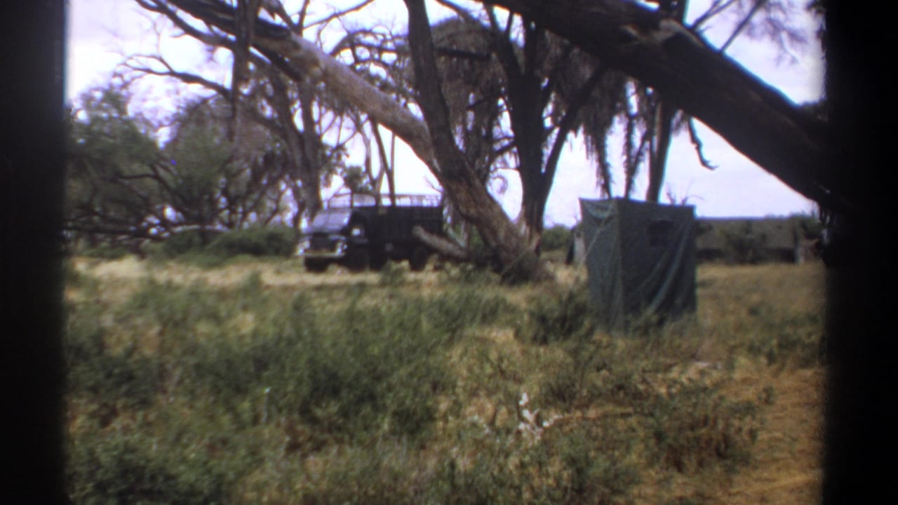 1969 Kenya home-movie frame showing tall grass, tree branches, a dark utility truck, and a small canvas tent at a bush camp.