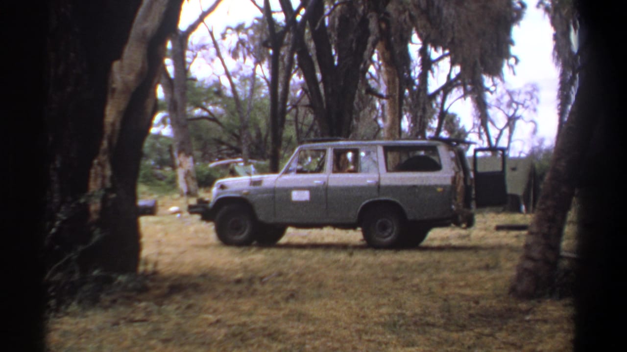 1969 Kenya 8mm frame showing a parked two-tone utility vehicle among trees, with a person visible inside.
