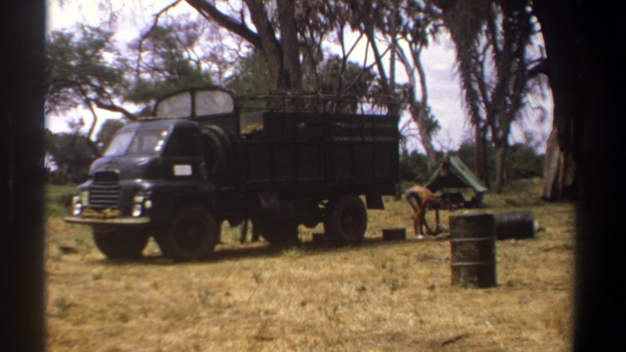 Black utility truck parked in a field while a man bends near a barrel and cargo.