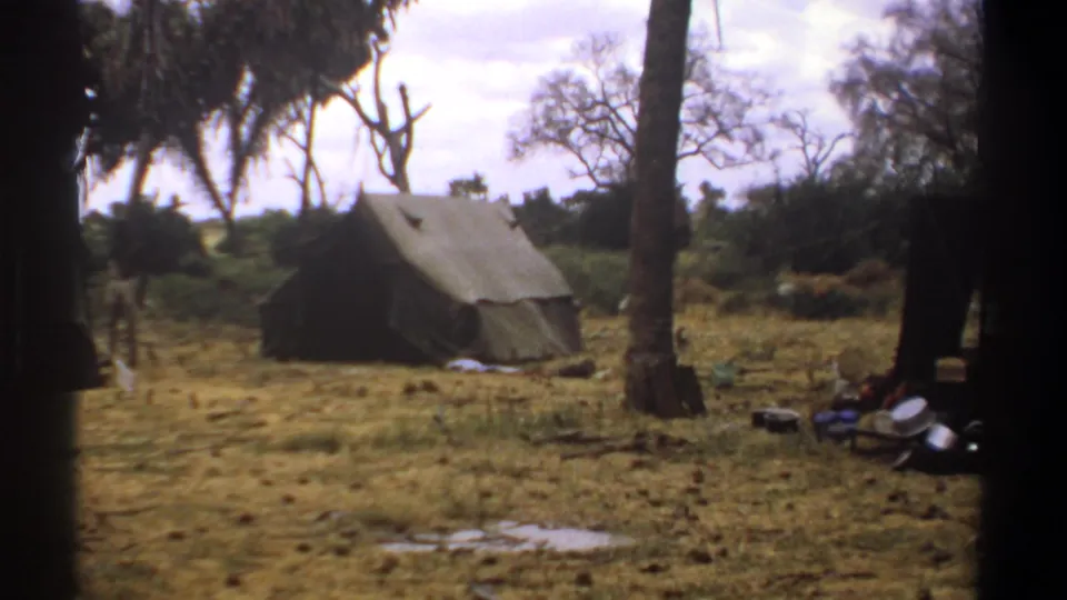 1969 Kenya 8mm frame centered on a canvas tent in a dry clearing, with trees and scattered camp equipment nearby.