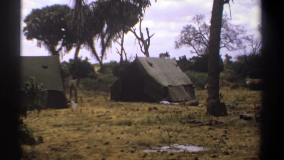 1969 Kenya 8mm frame of a green tent in a dry wooded campsite, with scattered gear and dark border from the film scan.