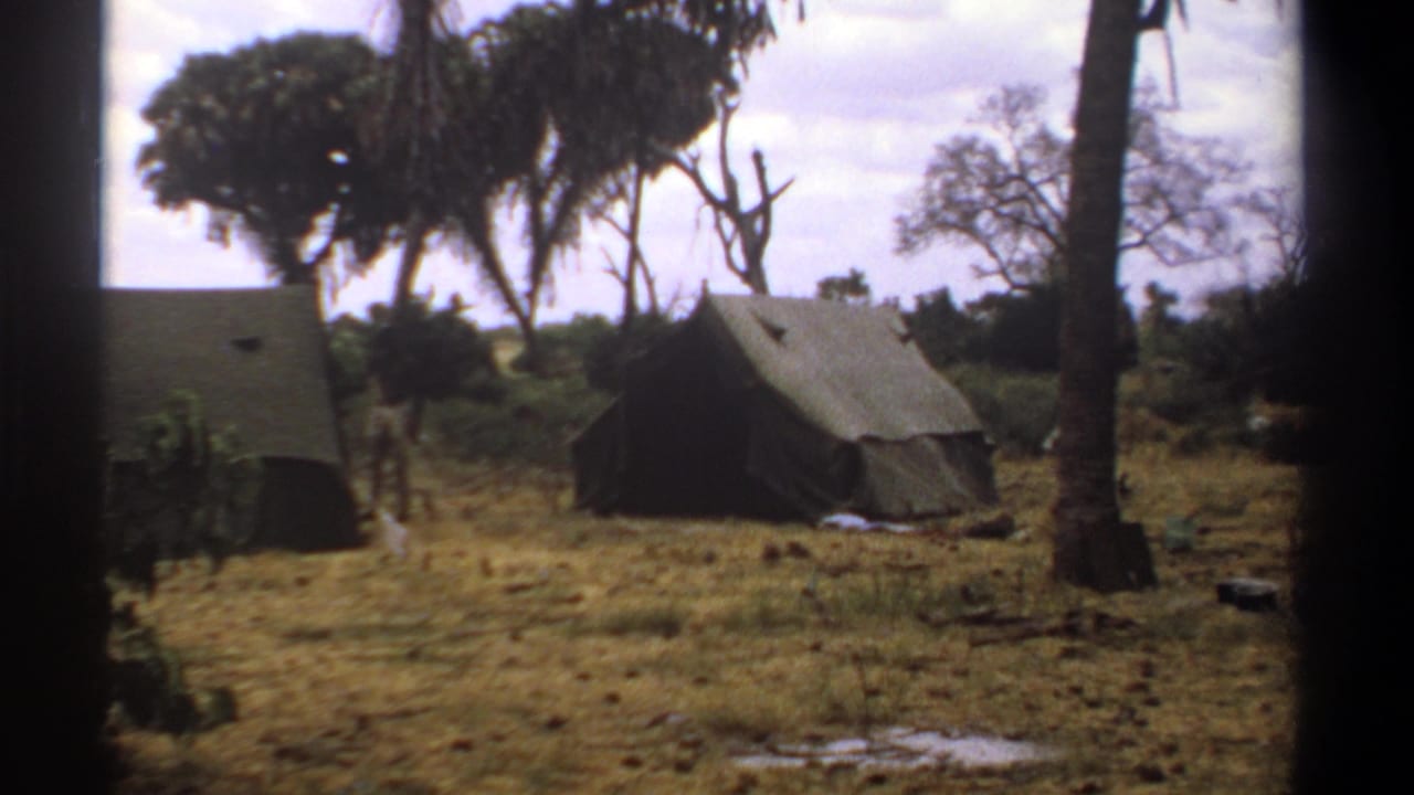 Canvas tents among dry grass and trees, seen through dark film-frame edges.