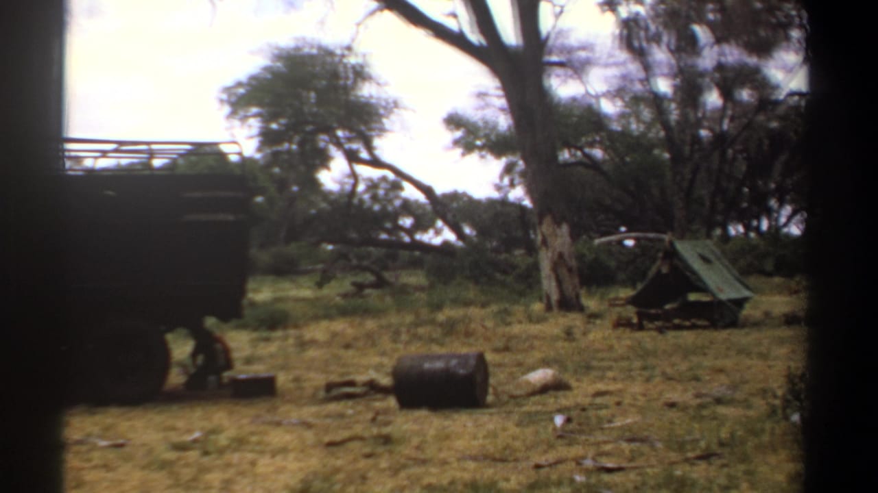 1969 Kenya 8mm frame showing a large truck, dry grass, trees, a small tent, and camp equipment in a rural campsite.
