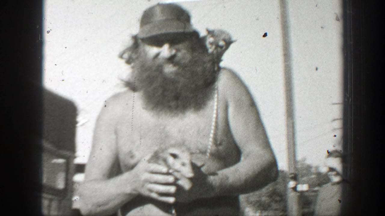 In 1939 California home-movie footage, a shirtless bearded man in a cap holds a small mouse-like animal while standing outdoors.