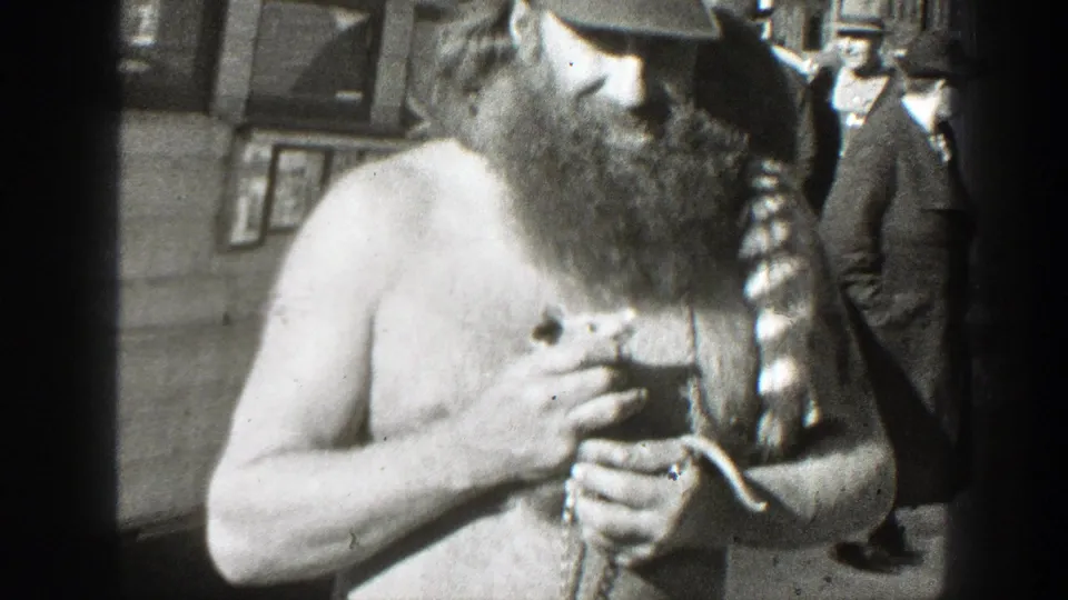 A closer street view shows the shirtless bearded man handling the small animal as an adult bystander stands in the background.