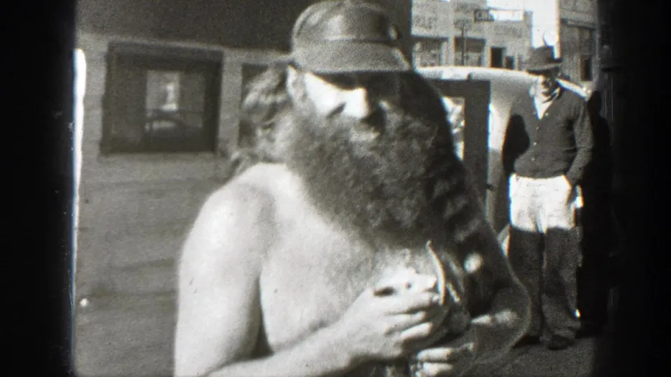 The man turns his body slightly in the California street scene, still holding the small mouse-like animal as onlookers stand nearby.