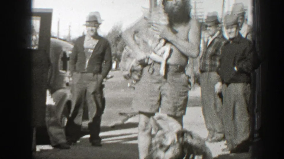 In 1939 California home-movie footage, a bearded shirtless man holds two turtles as adult men in hats stand around him outdoors.