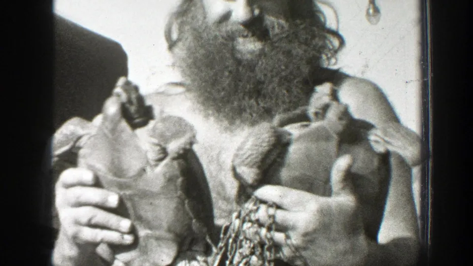 In 1939 California home-movie footage, a bearded shirtless man in a cap holds two large turtles close to the camera.