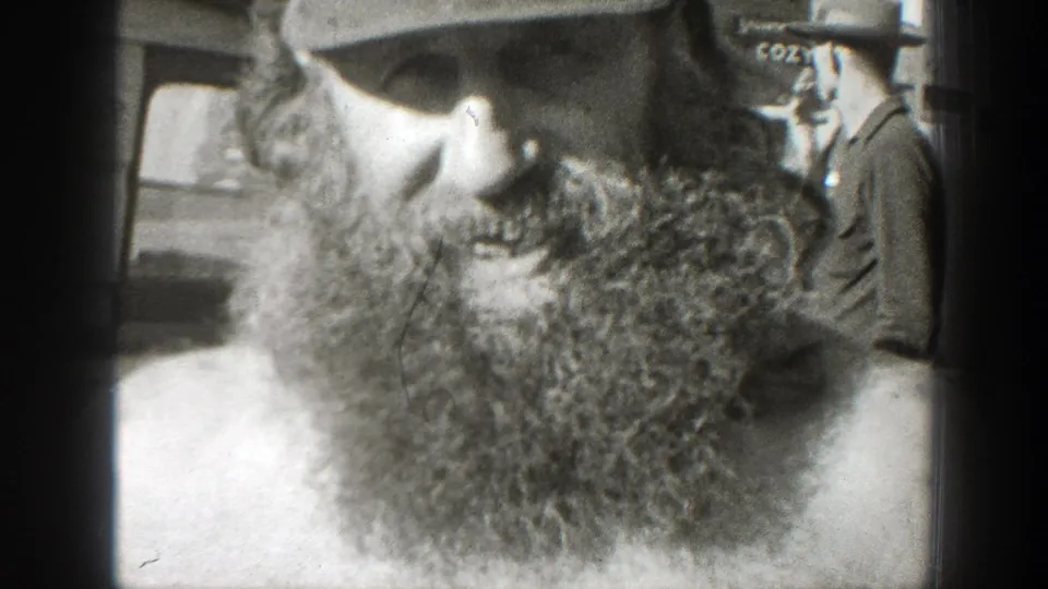 A 1939 California 8mm frame shows the bearded man leaning over a turtle while a partly visible person with lettering on a cap stands nearby.