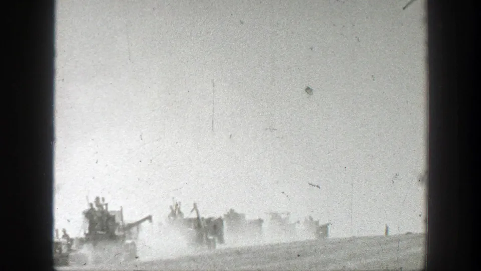 1939 California 8mm frame showing several distant harvest machines crossing a dusty field with operators visible as small figures.
