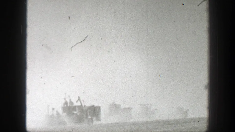 Soft black-and-white 8mm frame of harvest machines barely visible through dust across a California field in 1939.
