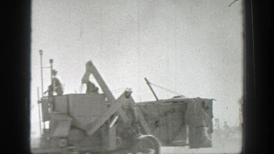 1939 California footage frame with soldiers riding a boxy military vehicle as dust hangs over the road.