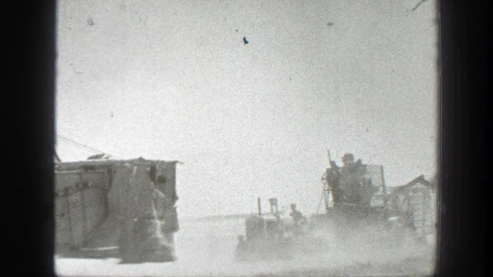 1939 California frame showing a military vehicle moving away through dust with soldiers and small roadside structures in view.