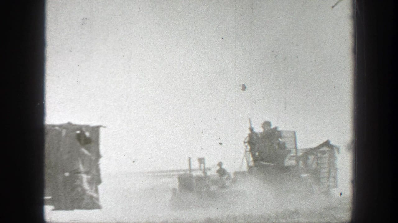 Dusty field machinery with several people visible under a bright sky.