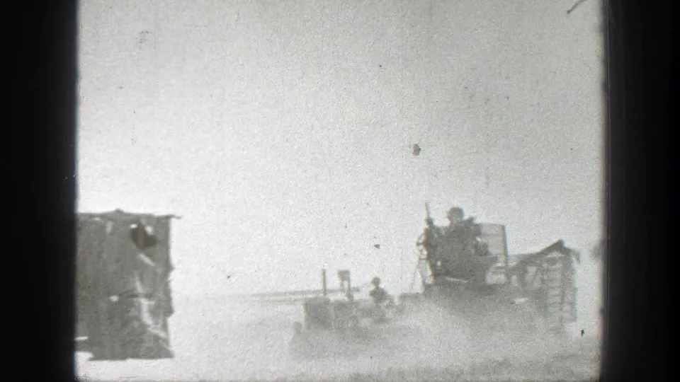 1939 California 8mm frame showing old farm machinery moving through dust with people riding or standing on the equipment.