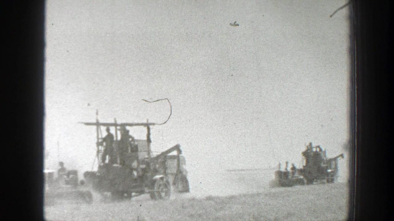 1939 California home-movie frame showing workers on two harvester machines moving through a dusty field beneath a bright, washed sky.