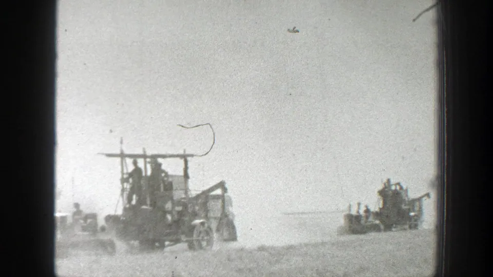 1939 California home-movie frame showing workers on two harvester machines moving through a dusty field beneath a bright, washed sky.