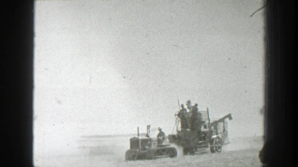 1939 California 8mm frame showing workers on and beside a harvester pulled through a bright dusty field.