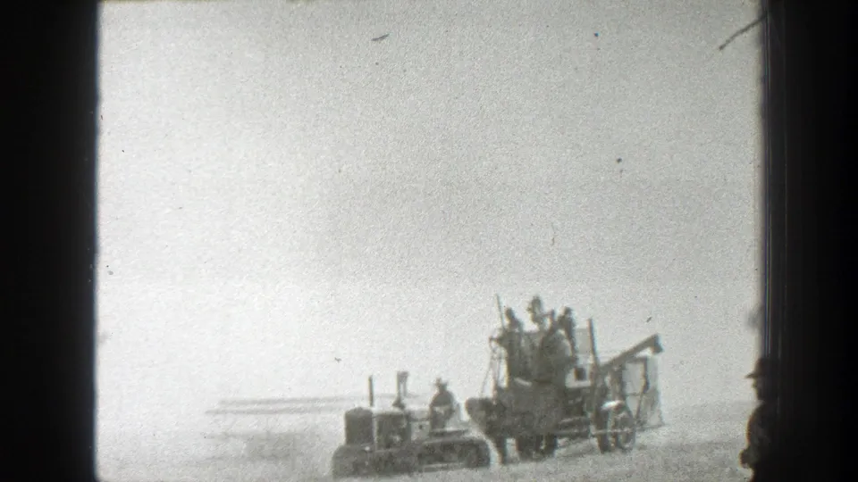 Distant 1939 California farm scene with a tractor-style unit pulling an open harvester carrying several workers.