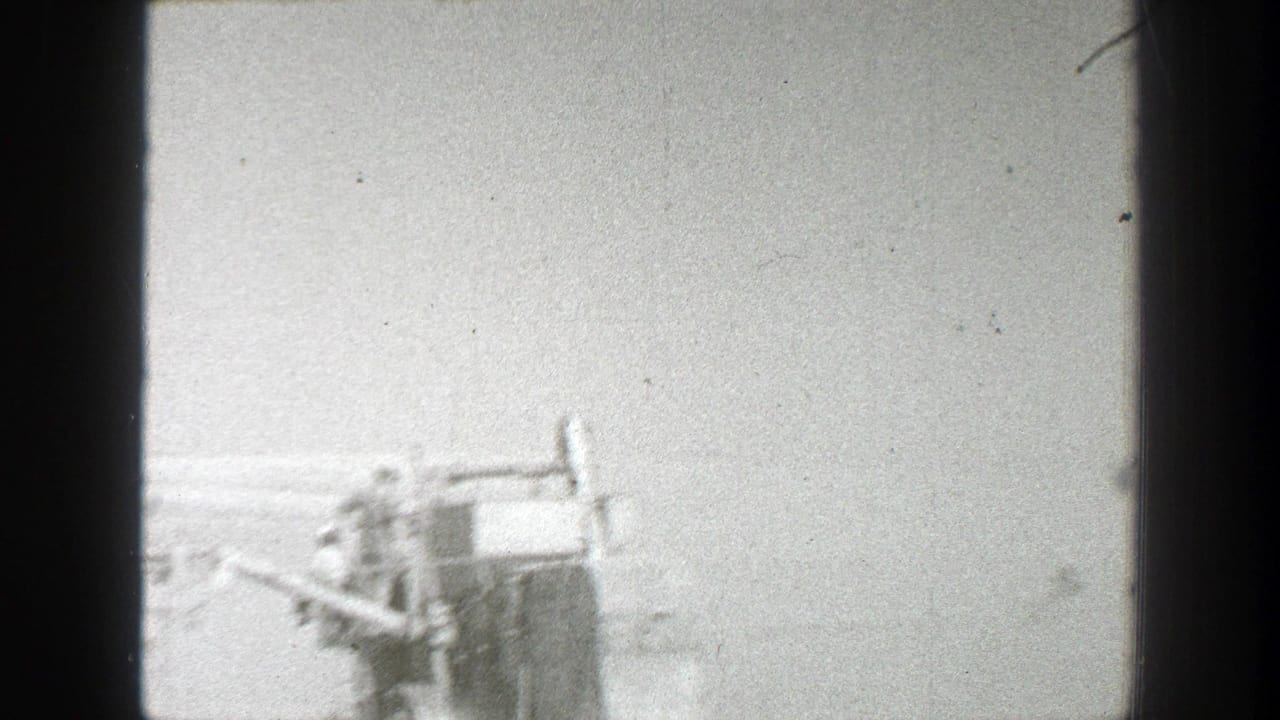 1939 California 8mm frame showing distant workers near partial farm machinery in a rural field, with soft black-and-white exposure.