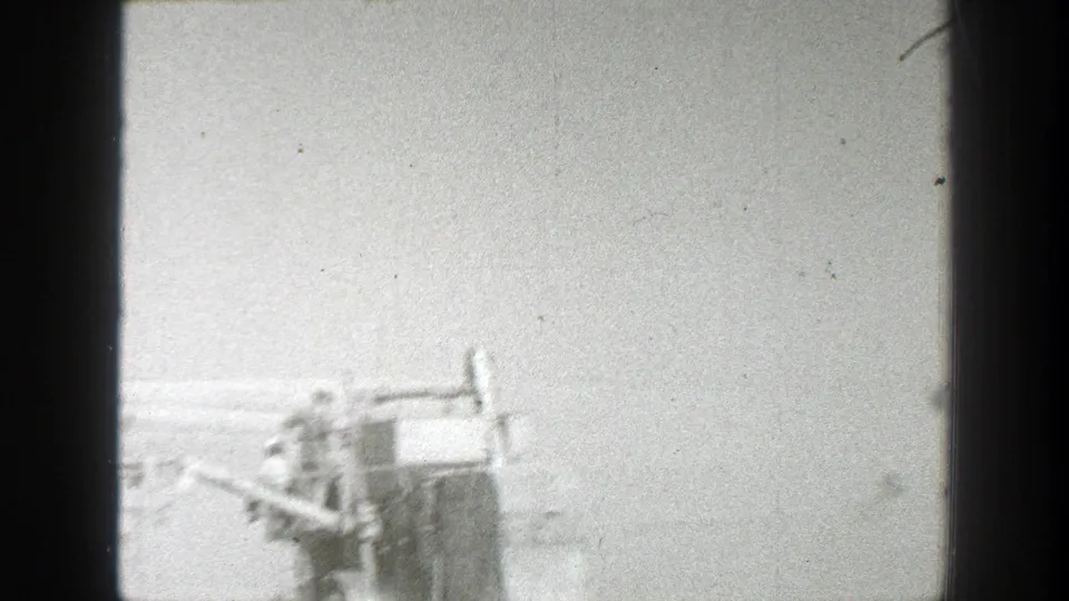 1939 California 8mm frame showing distant workers near partial farm machinery in a rural field, with soft black-and-white exposure.