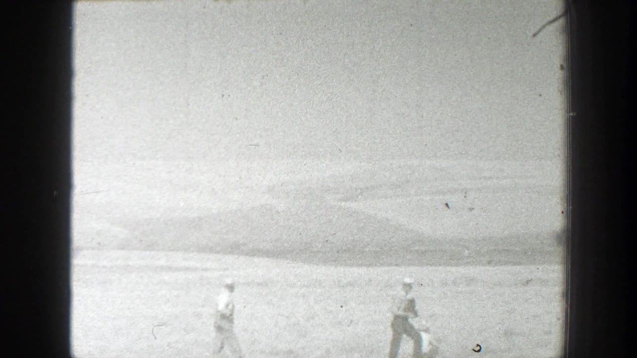 Two distant people walk across a pale open field under a low horizon.