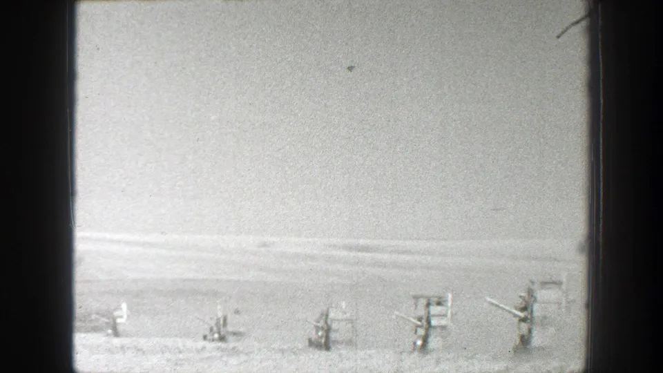 A distant figure stands among scattered field structures in an open California landscape, seen in soft 1939 home-movie footage.