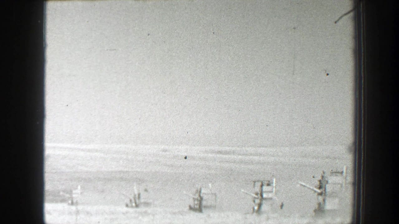 1939 California home-movie frame showing small farm machines spread across a flat field beneath a pale sky.