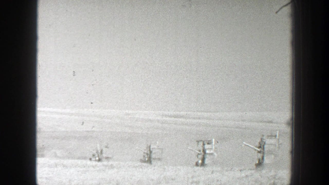 Distant soldiers stand in a snowy field behind small wooden structures.
