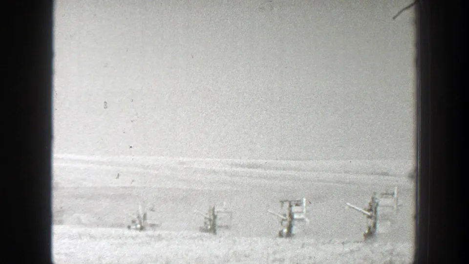 1939 California 8mm frame showing distant soldiers spaced across a snowy field near makeshift wooden firing positions.