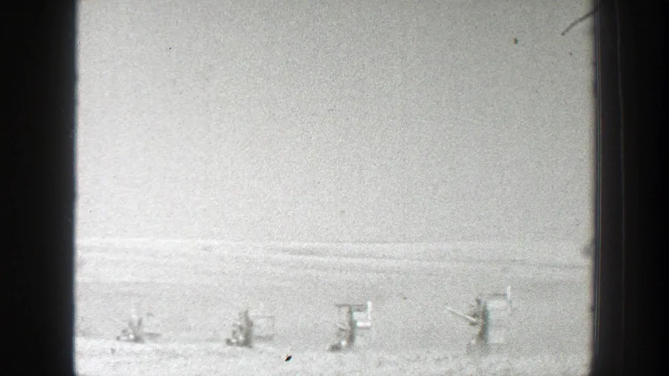 Distant uniformed figures in a 1939 California snowy field appear positioned for a military drill beside small wooden structures.