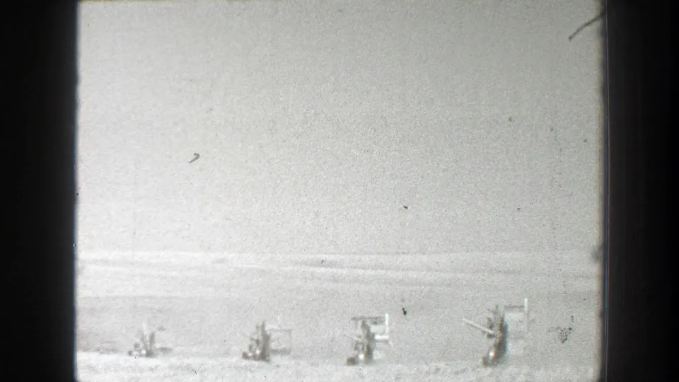 Black-and-white 8mm frame with visible gate border and distant soldiers along a snow-covered California training field.